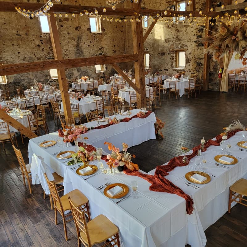 Long table with white linen and rust-colored florals in a barn