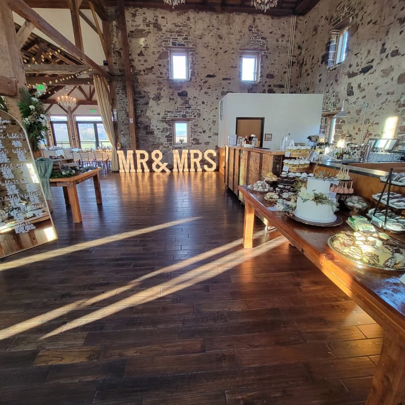 Stone barn reception with MR & MRS marquee letters, a dessert table and afternoon light across the floor