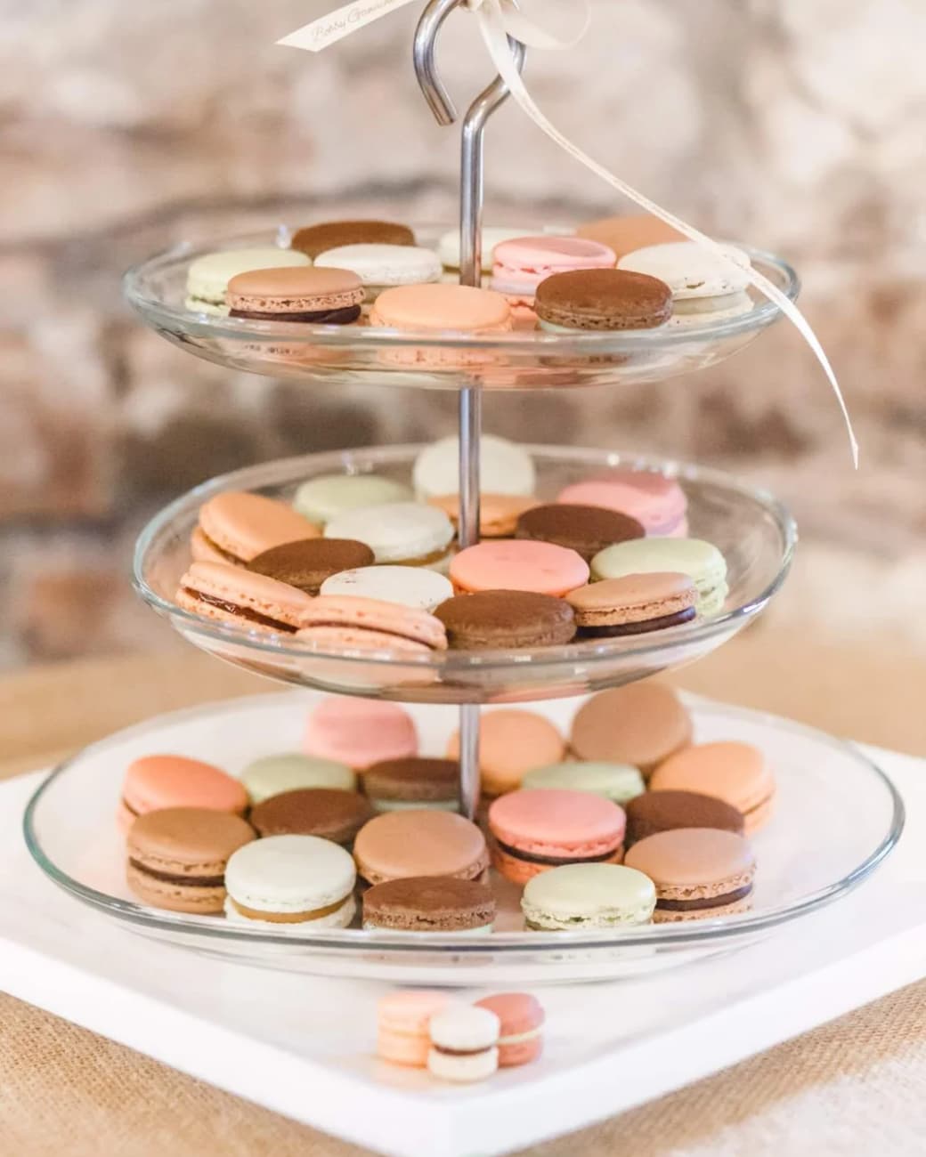 Three-tiered glass stand of pastel macarons tied with a ribbon